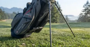 Automatic carbon-fiber retractable stand legs deploying smoothly on a lightweight golf bag for seniors on an uneven fairway.